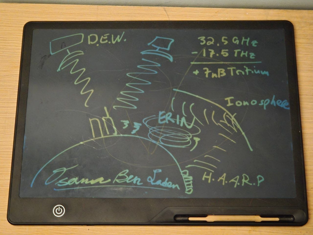 Parody photo of a digital drawing tablet with a scrawled conspiracy-style diagram: "D.E.W.", "Ionosphere", "H.A.A.R.P", "32.5 GHz - 17.5 THz + 7nB Tritium", and the signature "Osama Ben Laden".